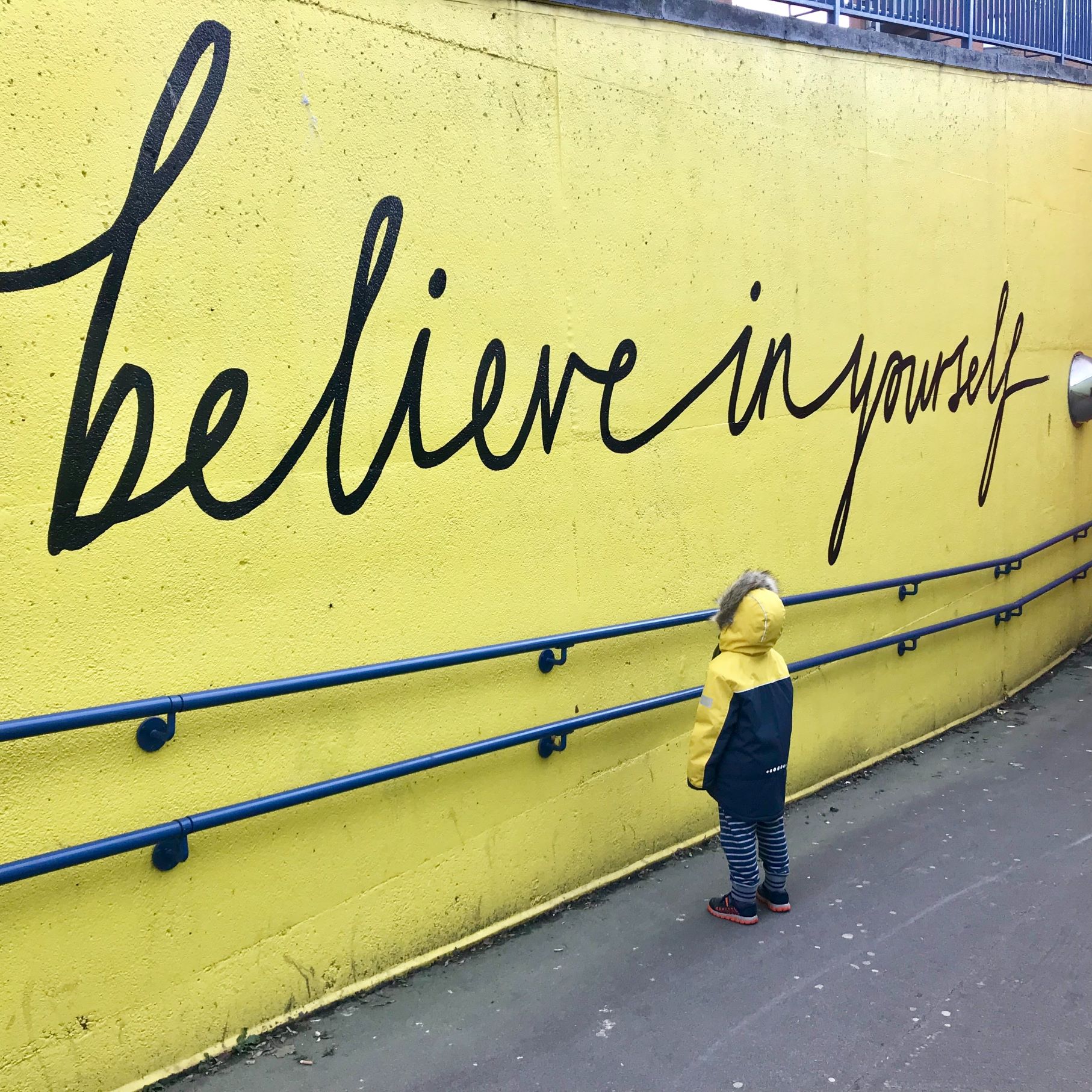 Kisfiú egy "Believe in yourself" (Higgy magadban) felirat előtt – az önbizalom és bátorítás fontosságának szimbóluma